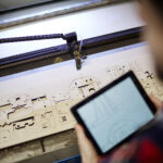 Plywood sheet with cut details and engineer with touchpad near by