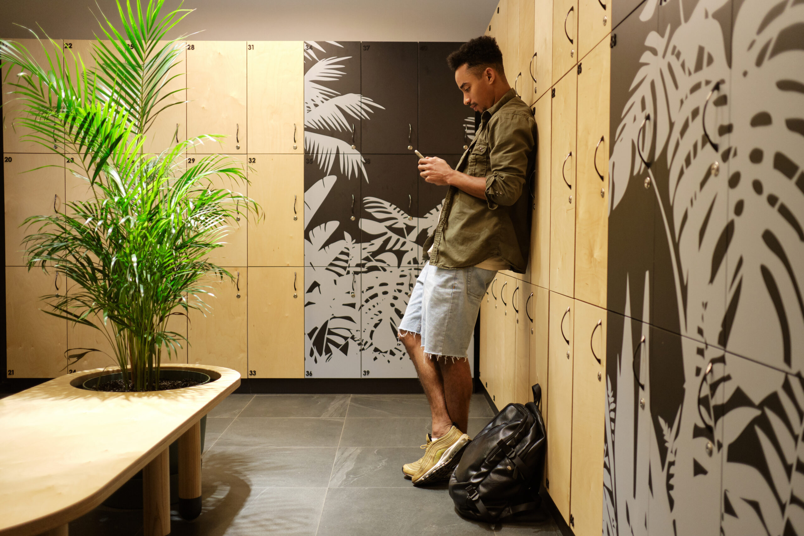 Young attractive serious casual African American man thoughtfully using cellphone in locker room